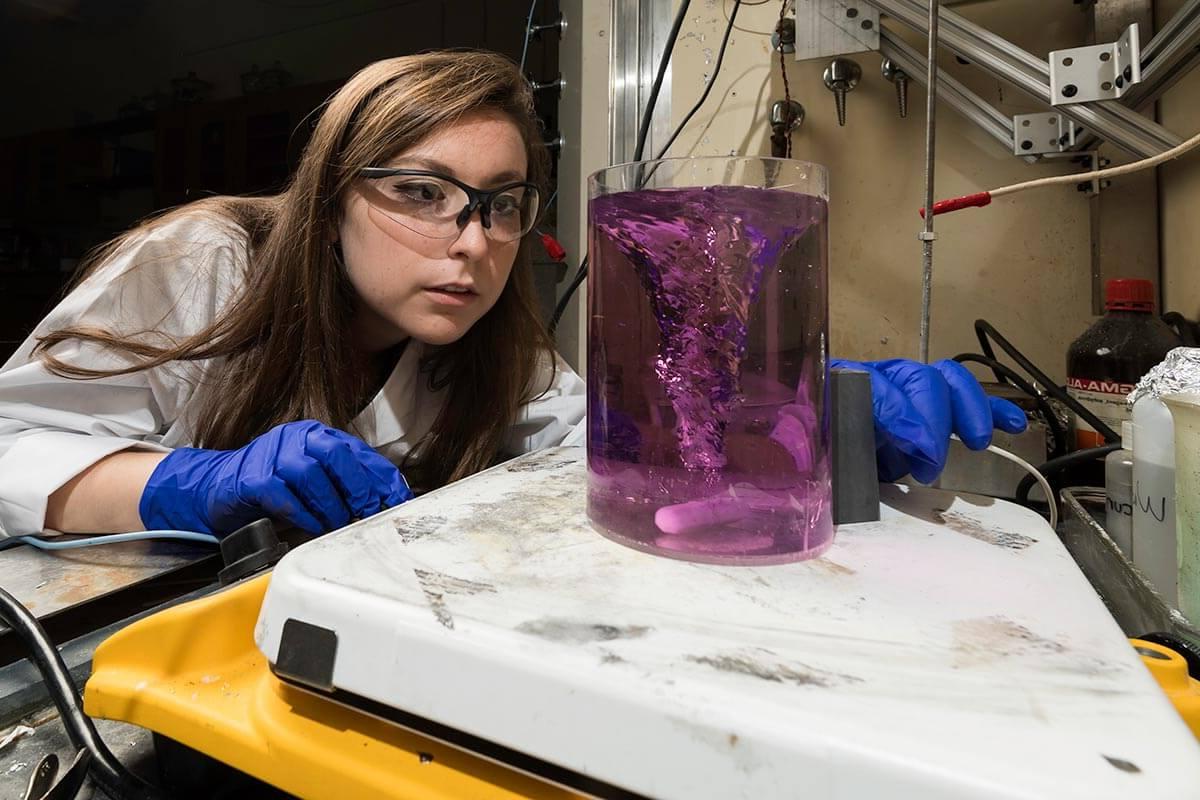 Student researcher looking at beaker of purple liquid in lab at University of Rochester 